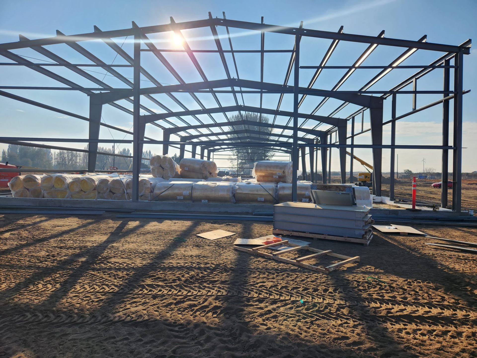 Large pre-engineered steel building frame at sunrise with insulation staged on site