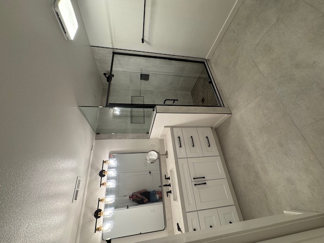 Bathroom remodel — single vanity with framed mirror beside a glass-enclosed tile shower